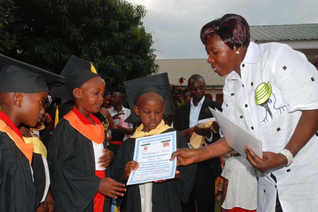 Noeline Nsungwa, the Headmistress for St. Christina Kindergarten in Hoima City hands over certificates to kids who had completed Nursery level. Credit: Robert Atuhairwe/The Albertine Journal.